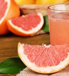 Eine Scheibe Grapefruit neben einem Glas frisch gepresstem Grapefruitsaft