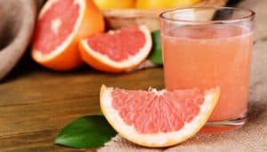 Eine Scheibe Grapefruit neben einem Glas frisch gepresstem Grapefruitsaft