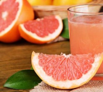 Eine Scheibe Grapefruit neben einem Glas frisch gepresstem Grapefruitsaft