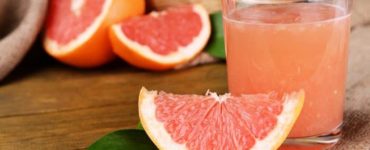 Eine Scheibe Grapefruit neben einem Glas frisch gepresstem Grapefruitsaft