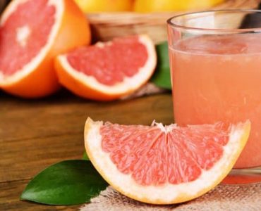 Eine Scheibe Grapefruit neben einem Glas frisch gepresstem Grapefruitsaft