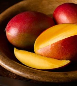 Eine in Scheiben geschnittene Mango, dahinter zwei ganze, rote Mangos