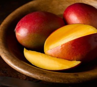 Eine in Scheiben geschnittene Mango, dahinter zwei ganze, rote Mangos