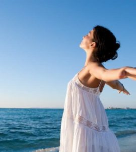 Frau mit geweiteten Armen steht am Strand