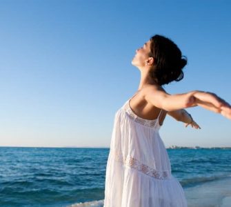 Frau mit geweiteten Armen steht am Strand