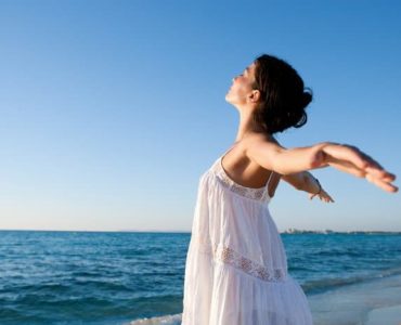Frau mit geweiteten Armen steht am Strand