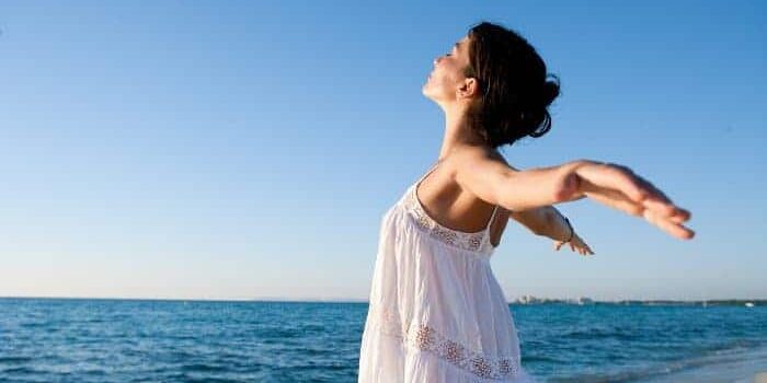 Frau mit geweiteten Armen steht am Strand