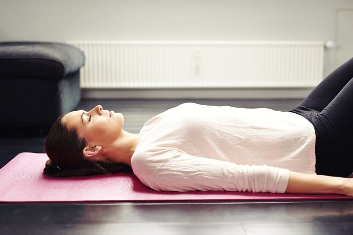 Progressive Muskelentspannung: Frau liegt mit Yogamatte im Wohnzimmer