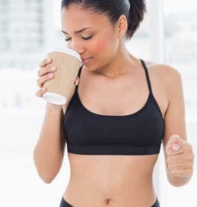 Dunkelhaarige Frau im Sportdress mit Kaffeebecher in der rechten Hand