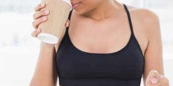 Dunkelhaarige Frau im Sportdress mit Kaffeebecher in der rechten Hand