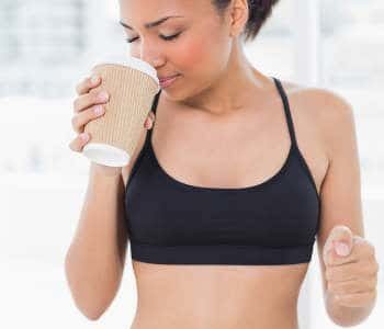 Dunkelhaarige Frau im Sportdress mit Kaffeebecher in der rechten Hand