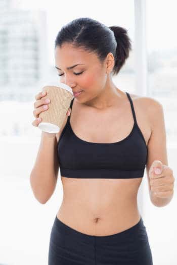 Dunkelhaarige Frau im Sportdress mit Kaffeebecher in der rechten Hand