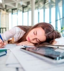 NAchmittagstief: Junge Frau im Büro liegt mit dem Kopf auf dem Schreibtisch und schläft