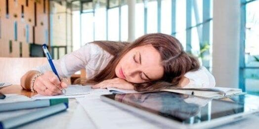 NAchmittagstief: Junge Frau im Büro liegt mit dem Kopf auf dem Schreibtisch und schläft