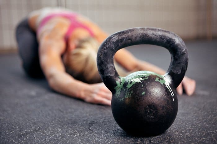 Blonde, Trainierte Frau liegt auf dem Boden, die Arme nach vorne ausgetreckt. Im Vordergrund liegt eine Kettlebell