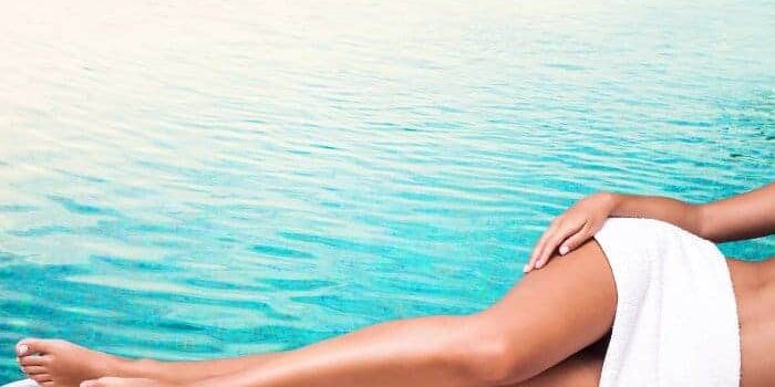 Schoenebeine Frau liegt seitlich vor einem Hintergrund mit türkisenem Wasser und streckt ihre schlanken, leicht gebräunte Beine seitlich aus.