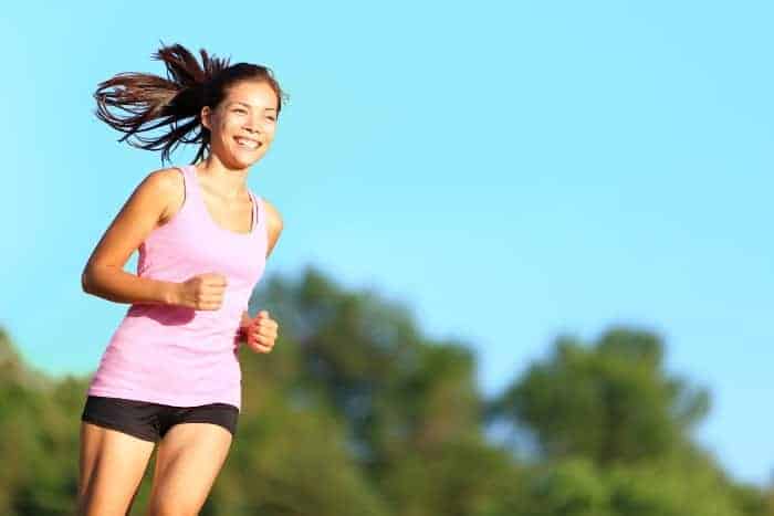 Junge Frau mit braunen Haaren und rosa Trägershirt lacht beim Jogging durch die Natur