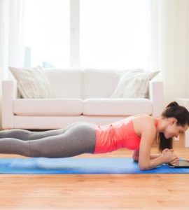 Frau macht eine Plank im Wohnzimmer auf einer Yogamatte vor einer Couch