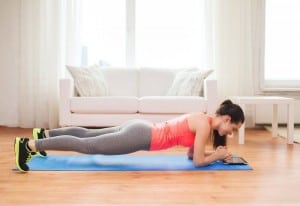 Frau macht eine Plank im Wohnzimmer auf einer Yogamatte vor einer Couch