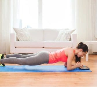 Frau macht eine Plank im Wohnzimmer auf einer Yogamatte vor einer Couch