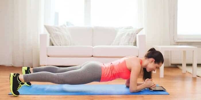 Frau macht eine Plank im Wohnzimmer auf einer Yogamatte vor einer Couch