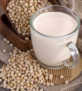 Eine durchsichtige Tasse gefüllt mit frischem Sojadrink umgeben von reifen Sojabohnen