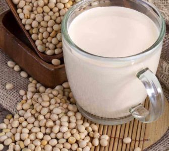 Eine durchsichtige Tasse gefüllt mit frischem Sojadrink umgeben von reifen Sojabohnen