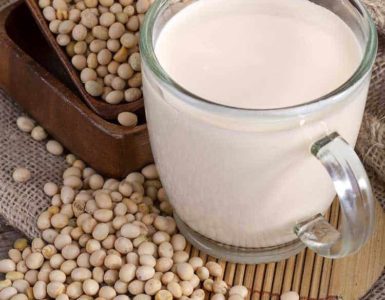 Eine durchsichtige Tasse gefüllt mit frischem Sojadrink umgeben von reifen Sojabohnen