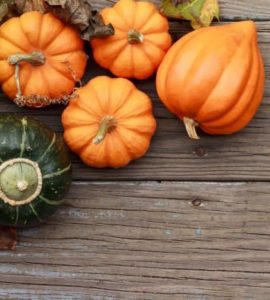 Vier orange und ein grüner Kürbis auf einem Holztisch