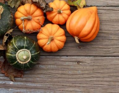 Vier orange und ein grüner Kürbis auf einem Holztisch