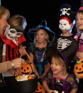 Frau verschenkt an in Halloweenkostümen verkleideten Kindern gesunde Süßigkeiten