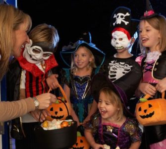 Frau verschenkt an in Halloweenkostümen verkleideten Kindern gesunde Süßigkeiten