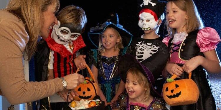 trick-or-treat Frau verschenkt an in Halloweenkostümen verkleideten Kindern gesunde Süßigkeiten