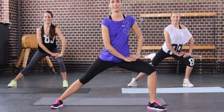 Drei Trainerinen mit bunter Kleidung machen seitliche Ausfallschritte bzw. Side Lunges