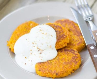 Drei Möhren-Couscous-Bratlinge mit Quark auf weißem Teller serviert