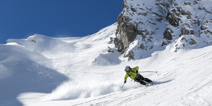 Mann in gelb-schwarzem Skianzug fährt mit Skiern eine Piste herab