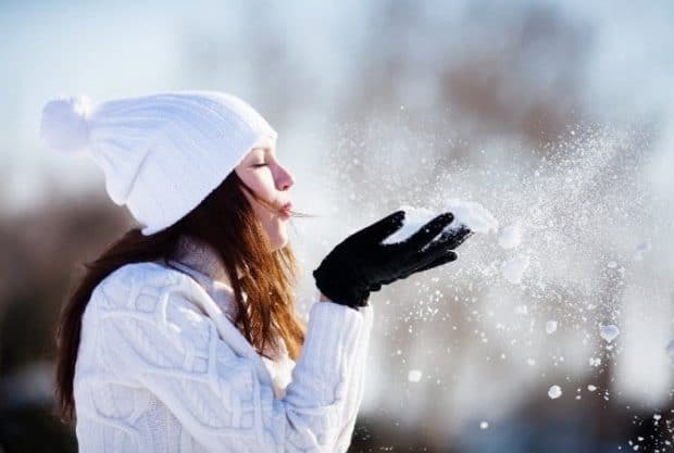 Frau mit weißer Mütze und Schal pustet Schnee aus ihren Händen