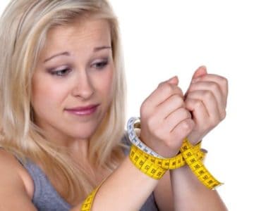 Blonde Frau mit Maßband als Fessel um die Handgelenke gewickelt