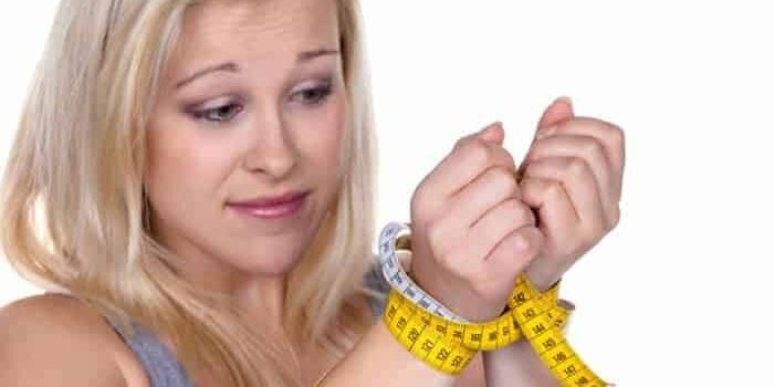 Blonde Frau mit Maßband als Fessel um die Handgelenke gewickelt