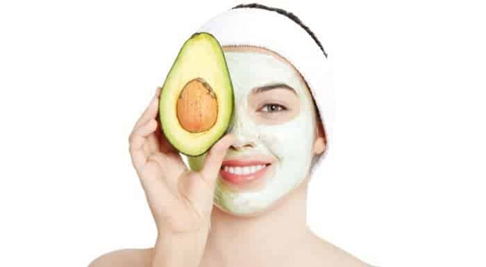 Frau mit Gesichtsmaske und halber Avocado