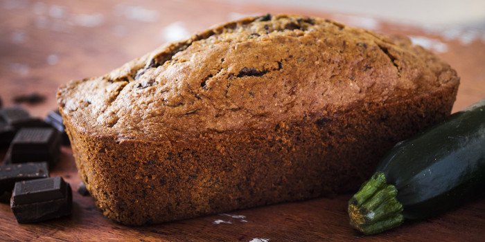 Schokoladen-Zucchini-Kuchen, umgeben von Stücken dunkler Schokolade und einer Zucchini