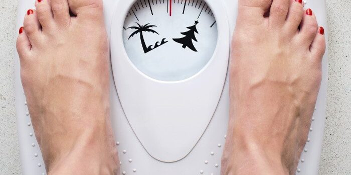 Frauenfüße mit rot lackierten Fußnägeln auf einer Waage, die eine Palme und einen Tannenbaum anzeigt