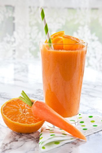 1 Glas A-C-E-Smoothie mit Strohhalm. Davor eine halbe Orange und eine Karotte