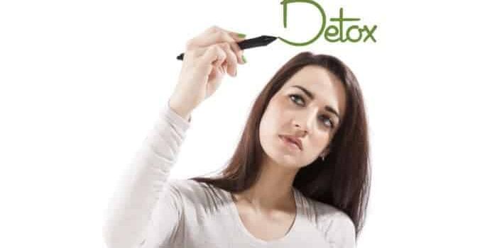 Junge Frau, die das Wort Detox auf eine virtuelle Glasscheibe schreibt