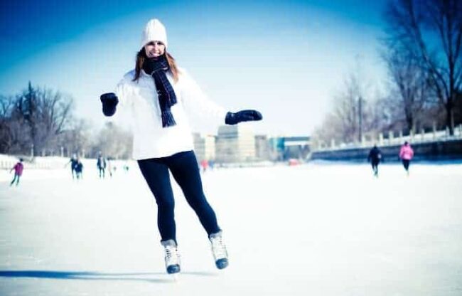 Frau in weißer Jacke und schwarzer Hose läuft Schlittschuhe auf zugefrorenem See