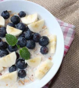 Keramikschüssel gefüllt mit Bananenstückchen, Blaubeeren und Molke, dazu etwas Minze