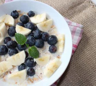 Keramikschüssel gefüllt mit Bananenstückchen, Blaubeeren und Molke, dazu etwas Minze