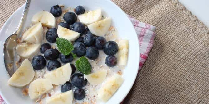 bananen-molke-mix Keramikschüssel gefüllt mit Bananenstückchen, Blaubeeren und Molke, dazu etwas Minze