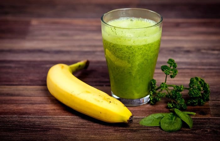 Ein Glas gefüllt mit Spinatsmoothie neben einer reifen Banane