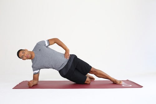Mann macht Side Plank mit abgesetztem Knie auf dunkelroter Trainingsmatte - Plank Varianten